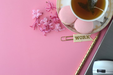 Top view of pink hyacinth, laptop, tea cup, cell phone and French macarons on pink background. Feminine workspace desktop with copy space.
