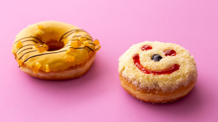 Close up of colorful and sweet donuts with one smiley face isolated on pink background