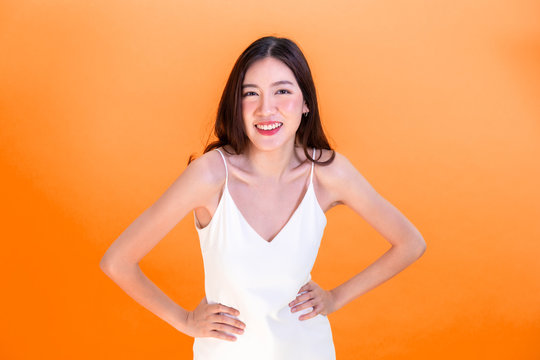 Asian Cute Woman Posing Arms Akimbo Or Hands On Hips Isolated On Orange Background