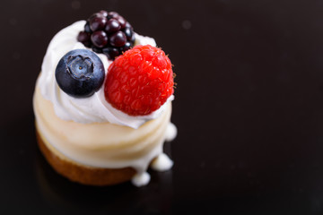 Mini cheesecake with berries and cream on a dark surface