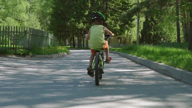Child riding bicycle at asphalt road in summer. Slow motion.