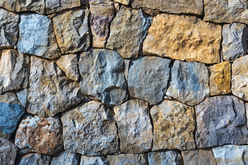 Colorful natural stone wall background with irregular blue and orange stones