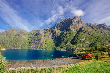 Red house on the shore of lake with view to mountains in the Norway at summer