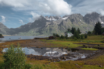 White house and mirror lake with view to snow mountains and sea in the Norway at summer