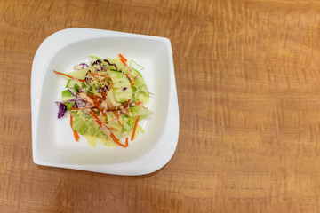 salad of fresh vegetables on a white porcelain plate on a brown wooden table