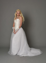 full length portrait of blonde girl wearing white corset gown. standing pose on grey studio background.