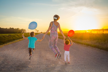 woman with children jumped on a rural road in the light of a sunset summer evening