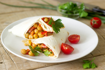 Burrito or shawurma with chickpeas, tomatoes and parsley on a light plate.