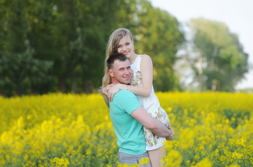 Naklejka na ściany i meble Happy young couple in love hugging in yellow colza field