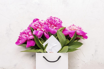 Peony bouquet in white bag and gift box on white background.