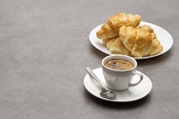 Cup of fresh coffee with croissants on dark background