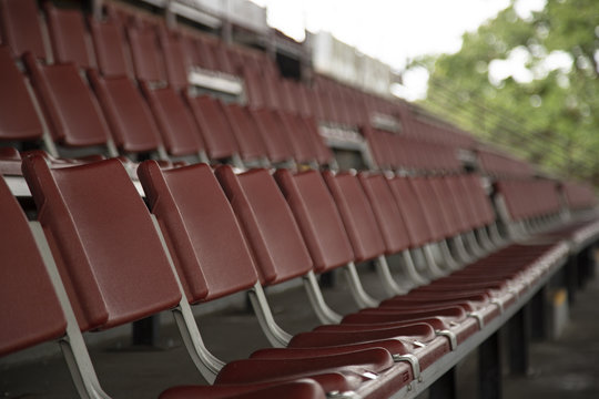 Rows of Empty Rust Colored Amphitheater Stadium Seats, Side Point of View with Pale Blue Sky and Trees in Background