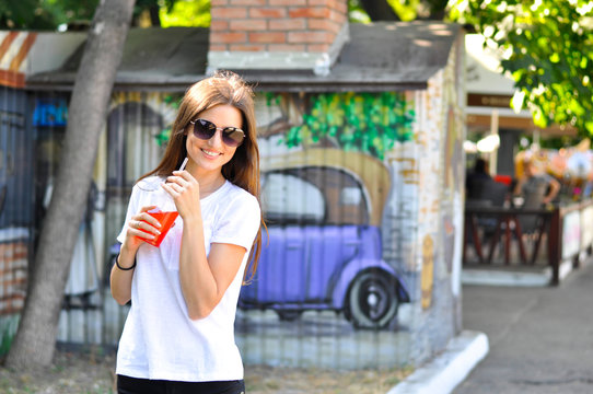 young attractive woman is walking around the city with a red cocktail (lemonade) in her hand