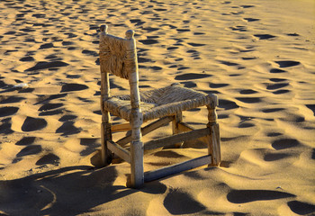 An old wicker chair from the vine is thrown out on an empty seashore against a background of yellow...