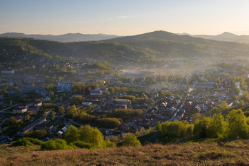 Fototapeta premium Green mountain landscape with illuminated sunset light town village valley among hills