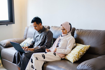 A portrait of a loving couple during Hari Raya festivital. They are Muslims and they decided to spend the day at home while relaxing on their living room couch.