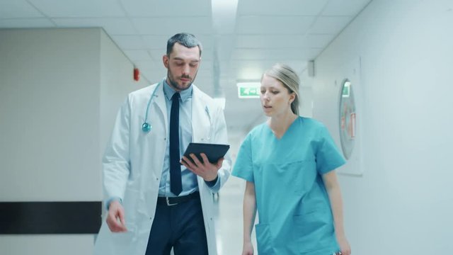 Surgeon and Nurse Walk Through Hospital Hallway, They Consult Digital Tablet Computer while Talking about Patient's Health. Shot on RED EPIC-W 8K Helium Cinema Camera.