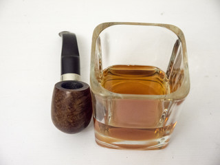 Briar smoking pipe near a glass of whisky close view with white background