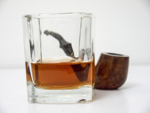 Briar smoking pipe behind a glass of whiskey close side view with distorted background
