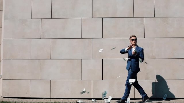 Young happy businessman scatter the dollars and funny dancing in the street. Money rain, falling dollars. It is located near the office center, slow motion. Successful business. Shot on Red Epic