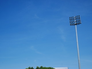 Sports light pole or Stadium Light tower in sport arena on blue sky with clouds.
