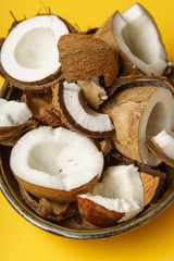 Cracked coconut and coconut pieces arranged in metallic tray on yellow background. Overhead view