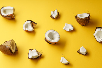 Cracked coconut and coconut pieces on yellow background. Overhead view
