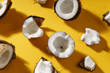 Cracked coconut and coconut pieces on yellow background. Overhead view