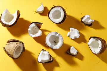 Cracked coconut and coconut pieces on yellow background. Overhead view