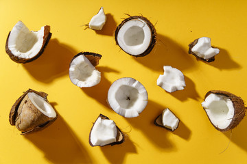 Coconut halves and pieces on yellow background. Food or cosmetics ingredient