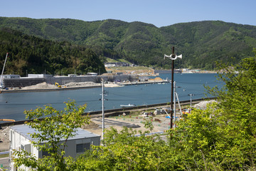 防災行政無線のスピーカーと堤防増設中の雄勝湾