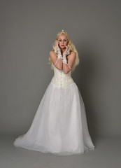 full length portrait of blonde girl wearing white corset gown. standing pose on grey studio background.