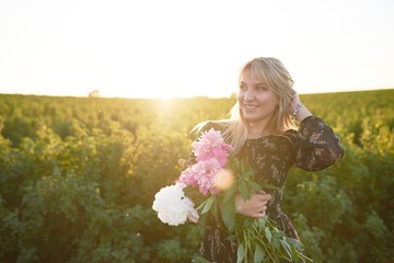 Cute young blonde girl spends time in a picturesque field with a bunch of pions in her hands