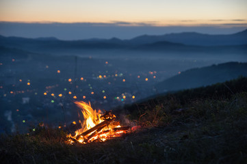 Fire on the mountain on the background of the bright sunset town village under a dark sky