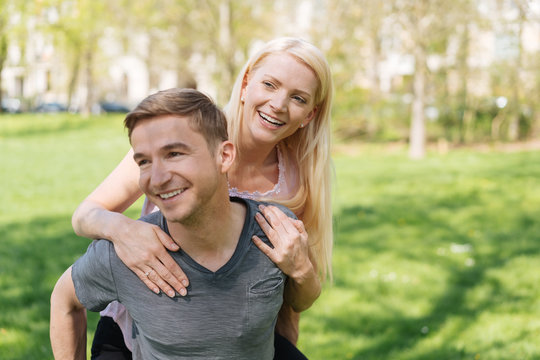 lachender Mann trägt seine Frau Huckepack durch den Park