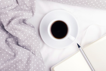 The cup of coffee and paper notebook with pencil on grey bed. Top view, morning mood concept.