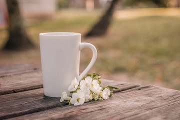 A white coffee cup on a weathered table next to a bouquet of white flowers.