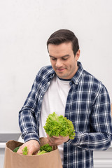 smiling adult man unpacking grocery store paper bag at kitchen