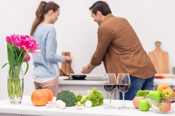 various vegetables and fruits on table at kitchen with blurred couple cooking dinner together on background