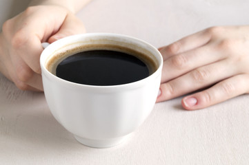 Hands holding a Cup of coffee on a bright table.