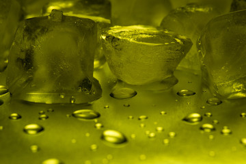 Ice cubes in lemon color on a reflecting table with drops of water