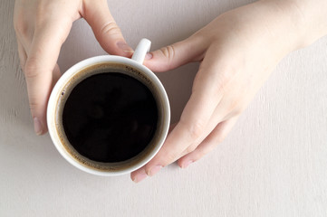 Hands holding a Cup of coffee on a bright table.