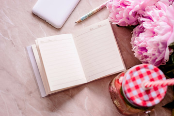 Beauty flat lay with a diary, smartphone, accessories and peonies on a marble background