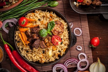 The concept of oriental cuisine. Homemade Uzbek pilaf from lamb served in cast iron cookware. Copy...