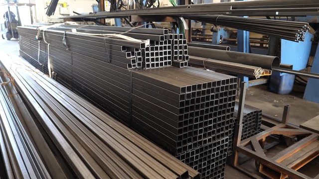 Stack of thick metal bars of iron in a factory warehouse. Forklift at work