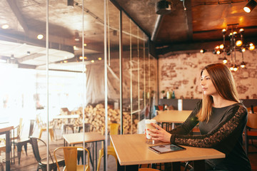 Young caucasian woman using tablet while sitting in cafe and drinking coffee.