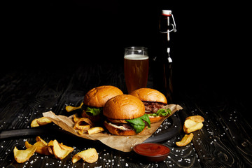 Set of junk food with burgers and french fries on table with beer in bottle and glass