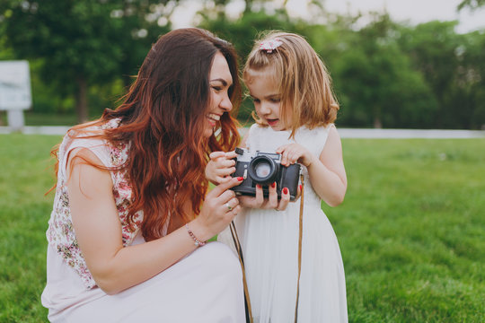 Joyful woman in light dress and little cute child baby girl take picture on retro vintage photo camera in park. Mother, little kid daughter. Mother's Day, love family, parenthood, childhood concept.