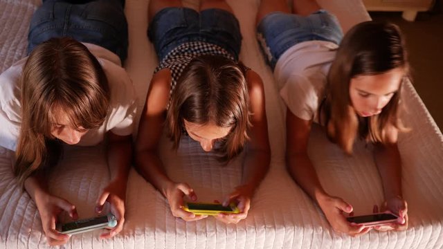 Type use smart phones chatting in social media three girls teenager sisters at home on bed in evening
