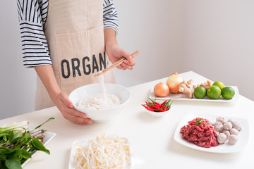 Female chef prepare traditional Vietnamese soup Pho bo with herbs, meat, rice noodles